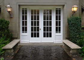 Elegant stone walkway bordered by stone benches leading to a double glass paned front door with two large front lanterns