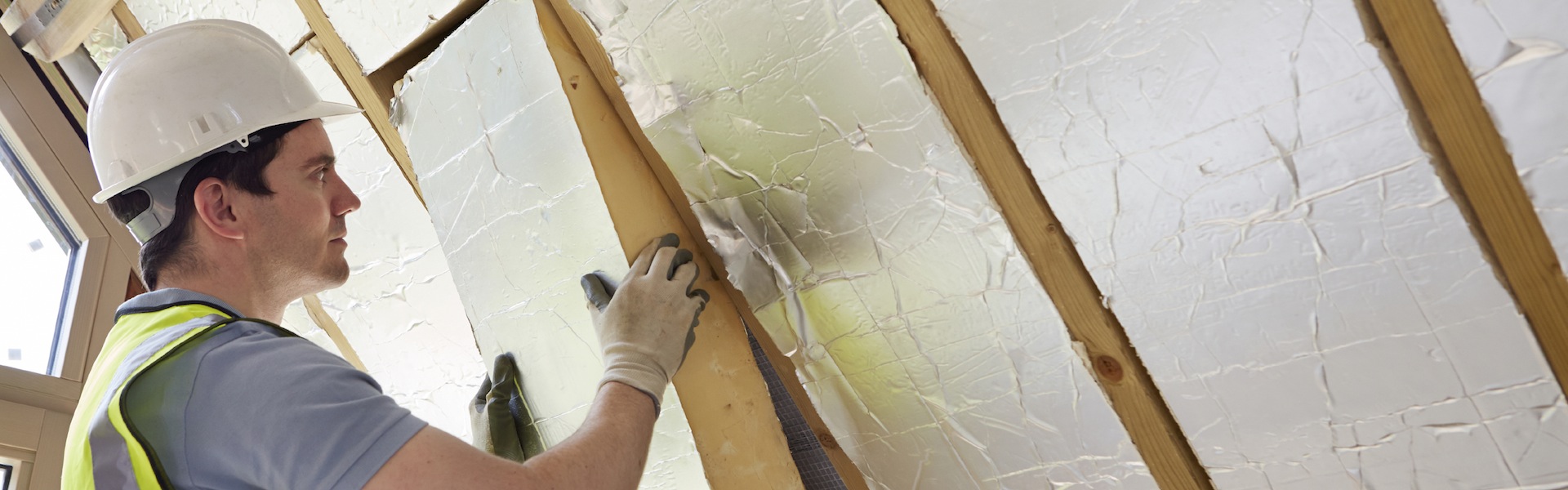 Builder Fitting Insulation Into Roof Of New Home