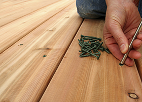 A hanywoman screws on new cedar decking.  Copy space on left.