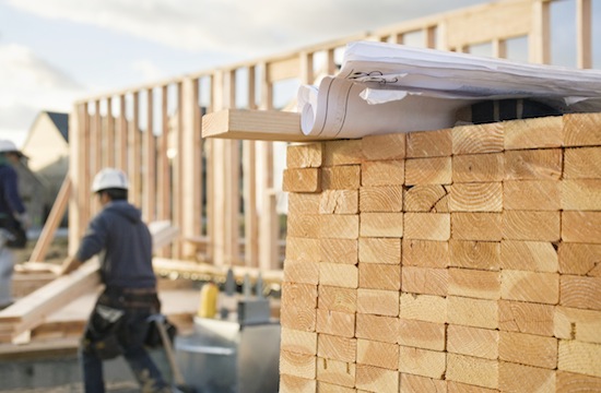 men working on a construction site and an upclose of wood stacked neatly